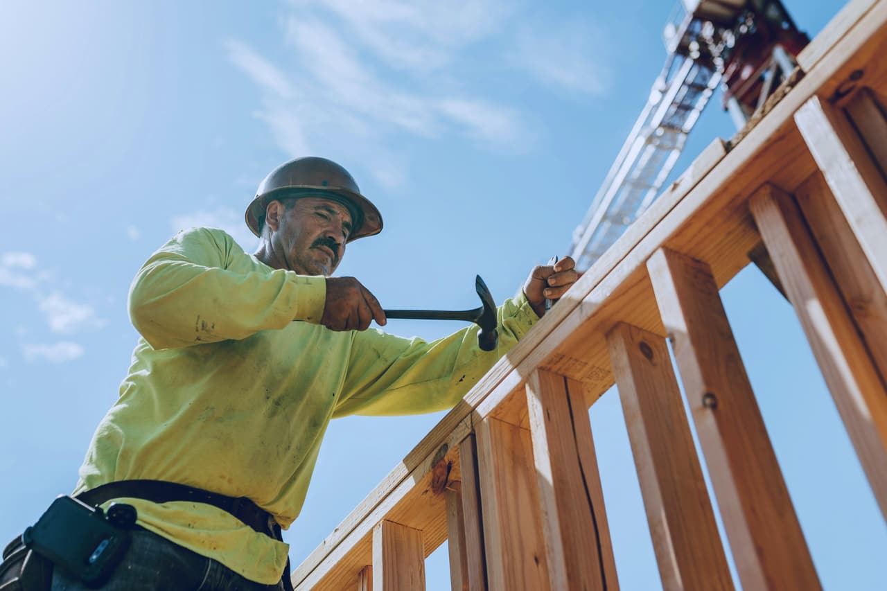 Framer in a hard hat nailing the top plate of a timber wall frame